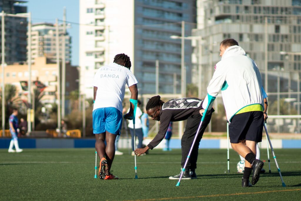 Jugador con discapacidad ayudando a un compañero sin discapacidad a ajustar las muletas antes de jugar.